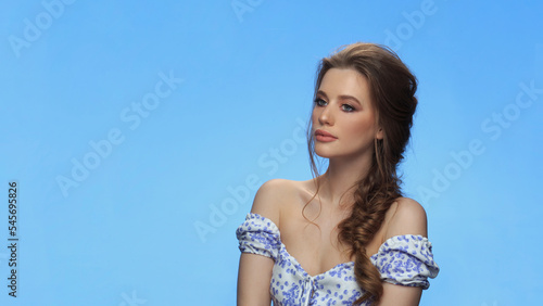Beautiful woman portrait beauty hair and skin makeup young model wear dress with bare shoulders, over blue background.