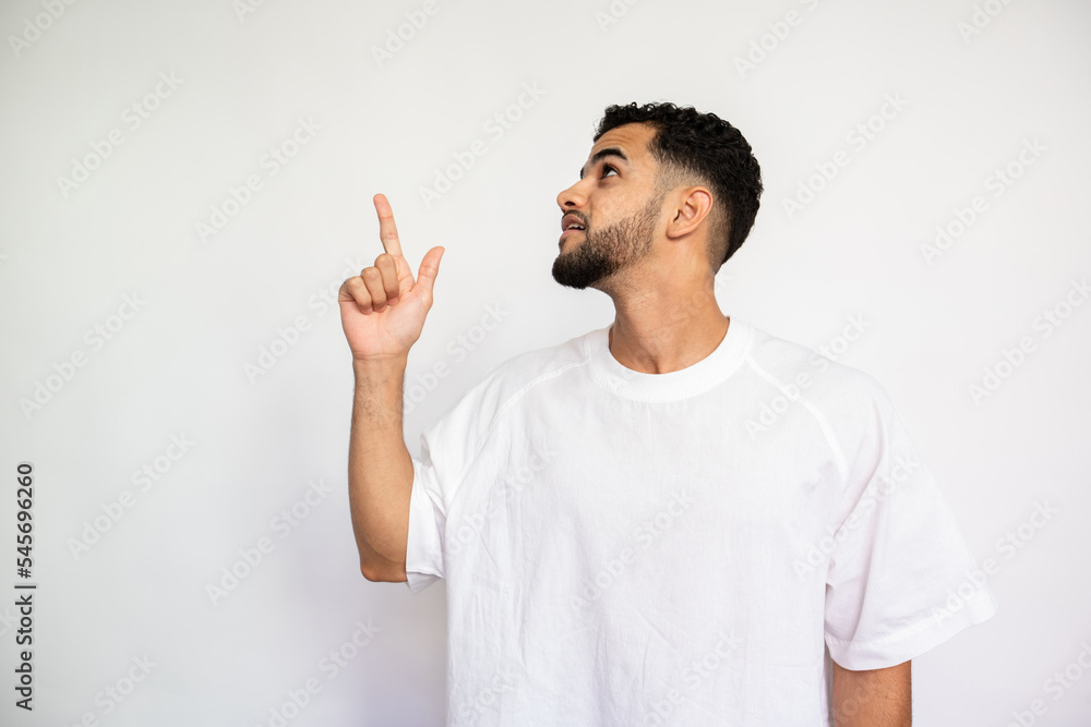 Portrait of confident young man pointing upwards over white background. Bearded man wearing white T-shirt showing something. Advertising concept Portrait of confident young man pointing upwards over white background. Bearded man wearing white T-shirt showing something. Advertising concept