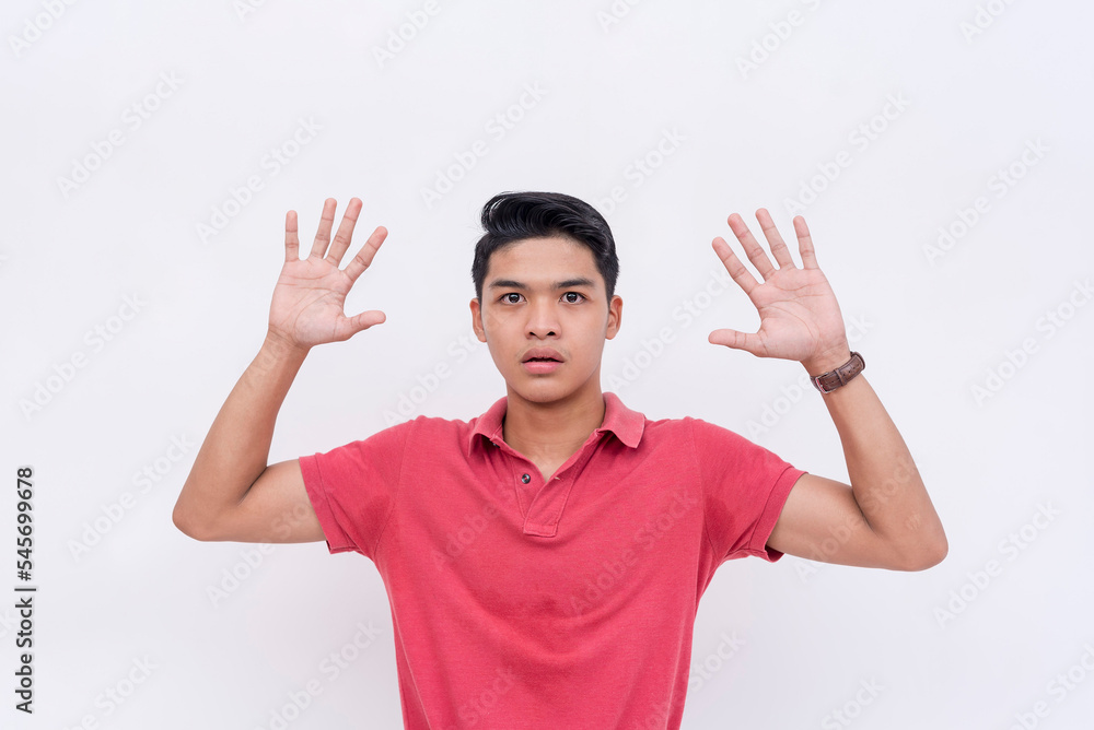 Naklejka premium A young man surrenders, putting both hands in the air. Yielding, being submissive or under arrest. Isolated on a white backdrop.