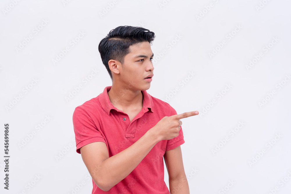A stunned young man points to something on the right while feeling speechless and shocked. Looking at something with wide eyes. Isolated on a white background. A stunned young man points to something on the right while feeling speechless and shocked. Looking at something with wide eyes. Isolated on a white background.