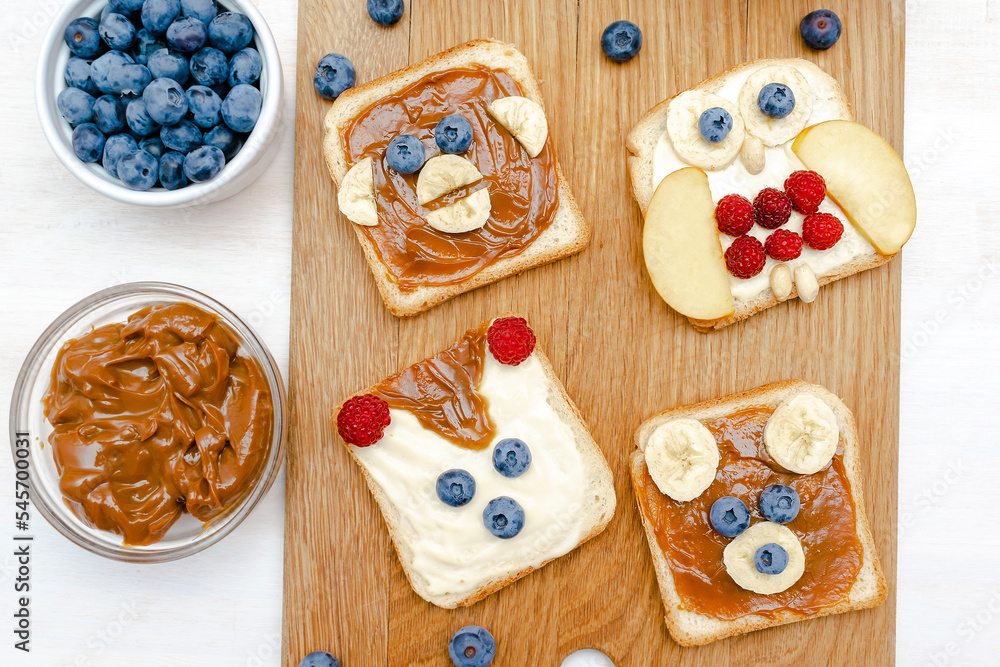 Funny cute bear,monkey,fox,owl faces sandwich toast bread with peanut butter,banana,blueberry,raspberry,milk. Kids childrens baby's sweet dessert healthy breakfast lunch food art,close up,top view.