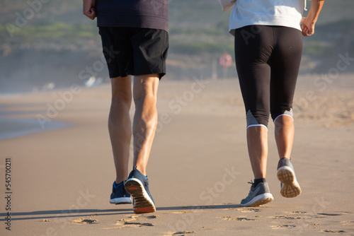 Back view of male and female legs jogging on seashore. Senior couple in sports clothes doing morning physical routine taking care of health. Sport as part of elderly peoples life concept