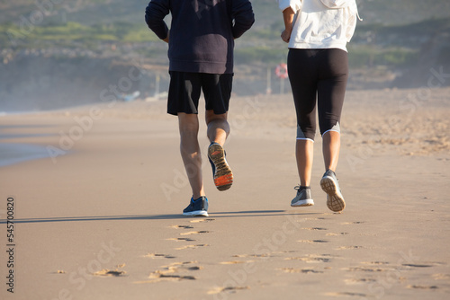 Back view of running elderly couple on sandy beach. Sporty man and woman training in morning jogging and breathing sea air. Sport, healthy lifestyle and stop aging for people concept