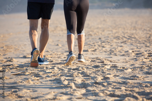 Man and woman jogging on sandy seashore on summer day. Back view of mature couple in sportswear and sneakers running in morning, working out together. Sport, fitness concept