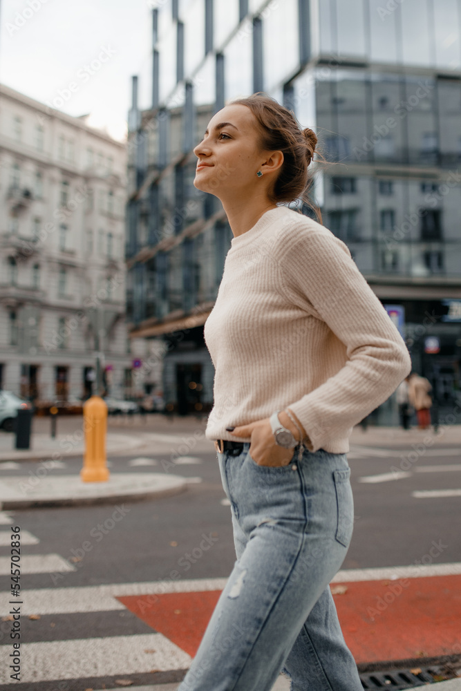 Cool girl in sweater looks away. Lifestyle portrait of a young stylish woman walking outdoors. Walk in Warsaw. Lifestyle portrait of a young woman in sweater standing on the street in Warsaw.