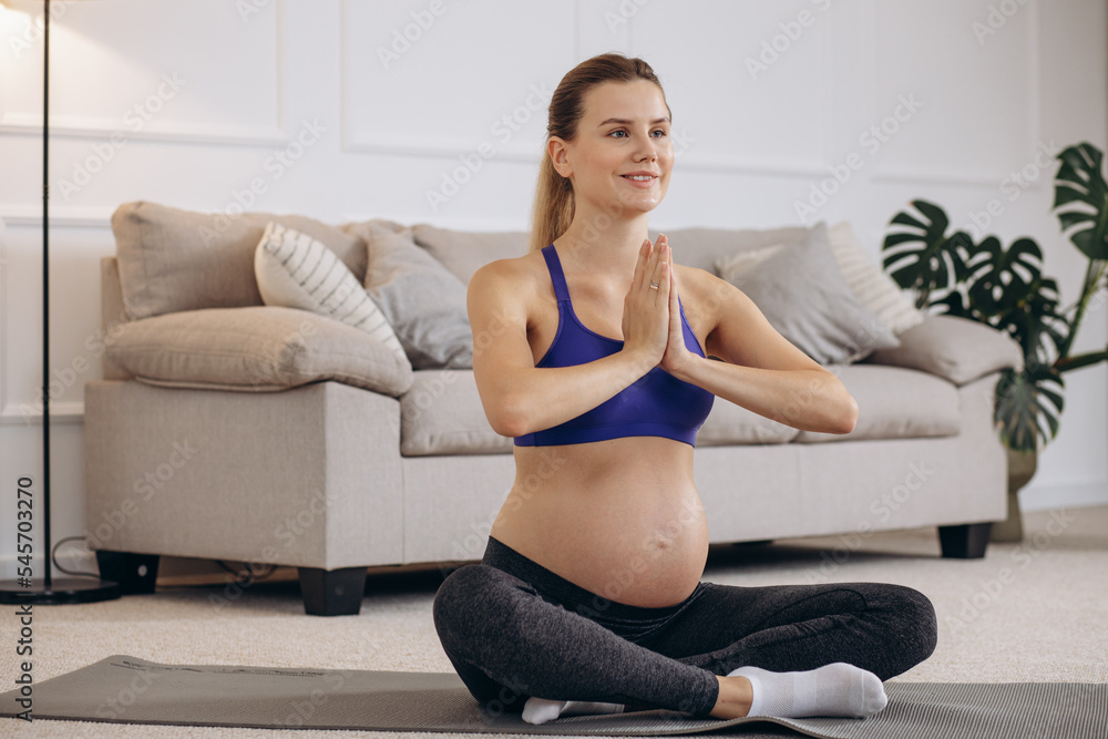 Pregnant woman practicing yoga at home on mat