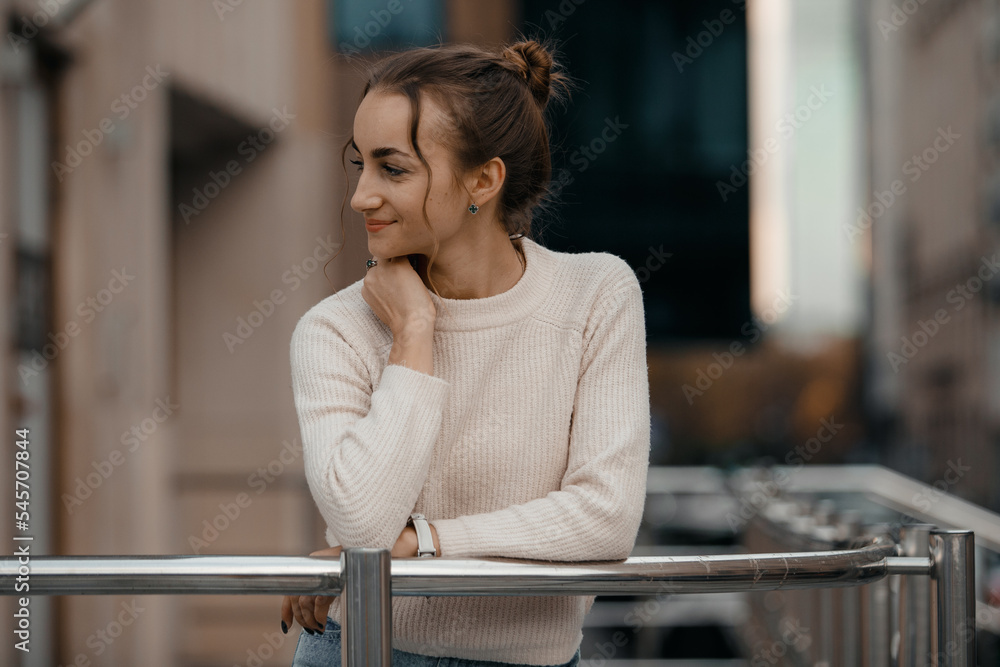 Professional woman worker wear standing outdoor terrace with a smile leaning on railing enjoy view from modern office skyscraper. Tall stylish girl near the railing and steps on the city background.