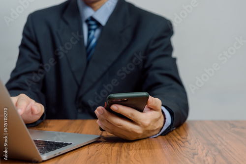 Business man working on laptop computer and using mobile phone on desk.