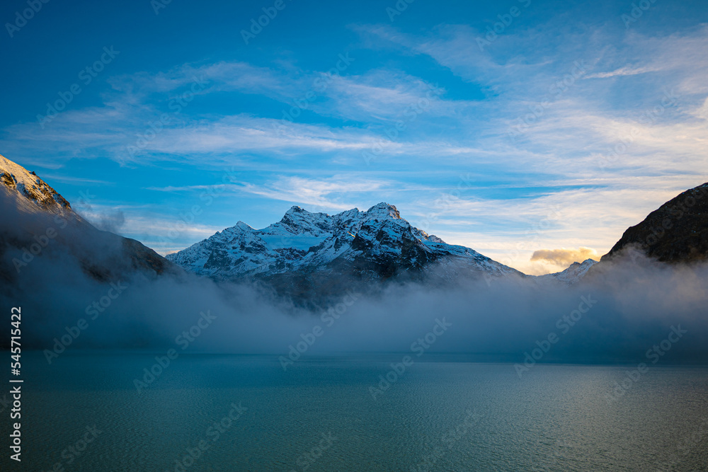 Mountain rising above the clouds with a calm lake in front