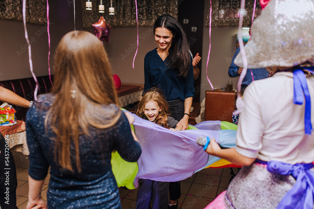 Little preschool girl, child and her mother, woman dancing, spinning indoors in a competition with a long multi-colored cloth of the animator in honor of the birthday. Little preschool girl, child and her mother, woman dancing, spinning indoors in a competition with a long multi-colored cloth of the animator in honor of the birthday.