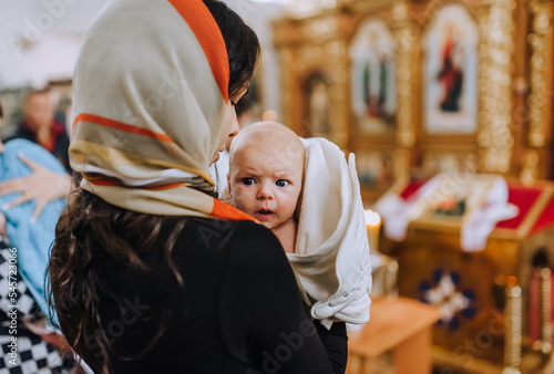 A young woman, mother holds a newborn baby in her arms in the church after the ceremony, ritual, rite of baptism. Photography, religion. photo