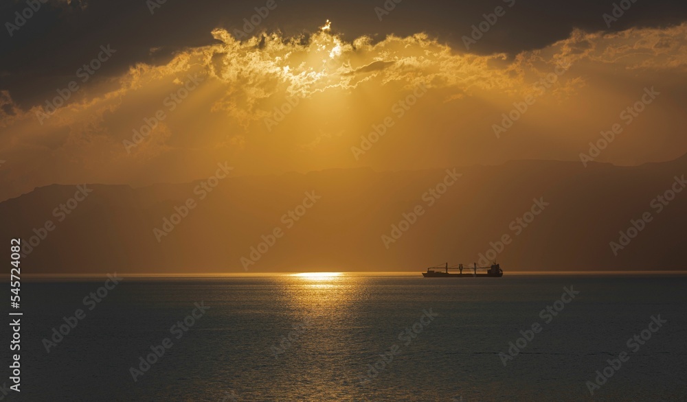 Bright golden sunset sky over a calm sea with an industrial ship
