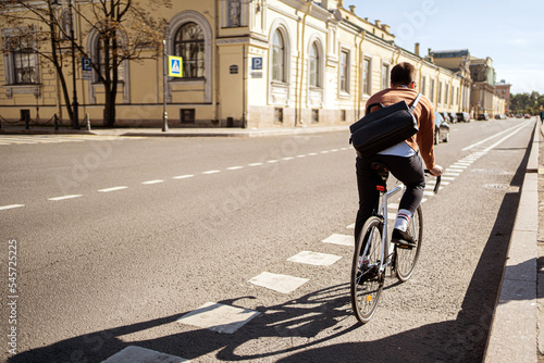 A male cyclist rides to work with a briefcase on a bicycle in the city. Ecological transport is modern. © muse studio