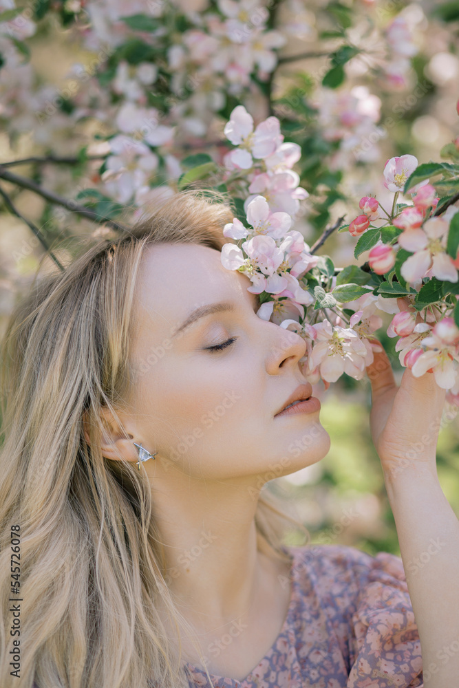 Naklejka premium Portrait of a beautiful woman who smells flowers, blooming apple orchard, long blond hair, spring time