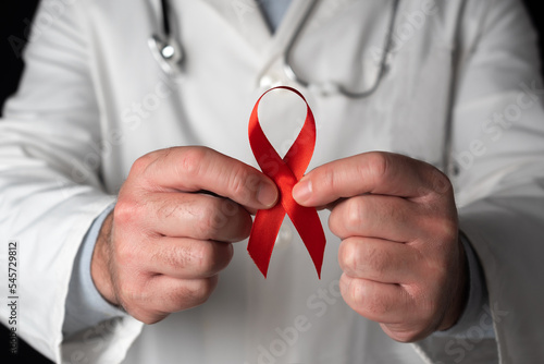 Close-up of a doctor holding a red ribbon with both hands, symbol of World AIDS Day. Support from health personnel to people with hiv. Prevention and fight against the AIDS virus