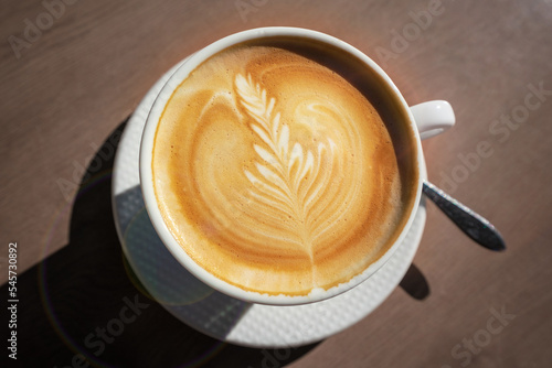 Fresh cappuccino cup with drawn leaf standing on wooden table of street cafe top view
