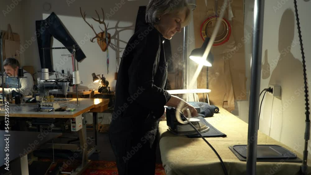 A female tailor seamstress working in a workshop repairing old vintage jeans on authentic sewing machines. Small family business, tailoring and repair of clothes, handmade, couturier, tradition A female tailor seamstress working in a workshop repairing old vintage jeans on authentic sewing machines. Small family business, tailoring and repair of clothes, handmade, couturier, tradition