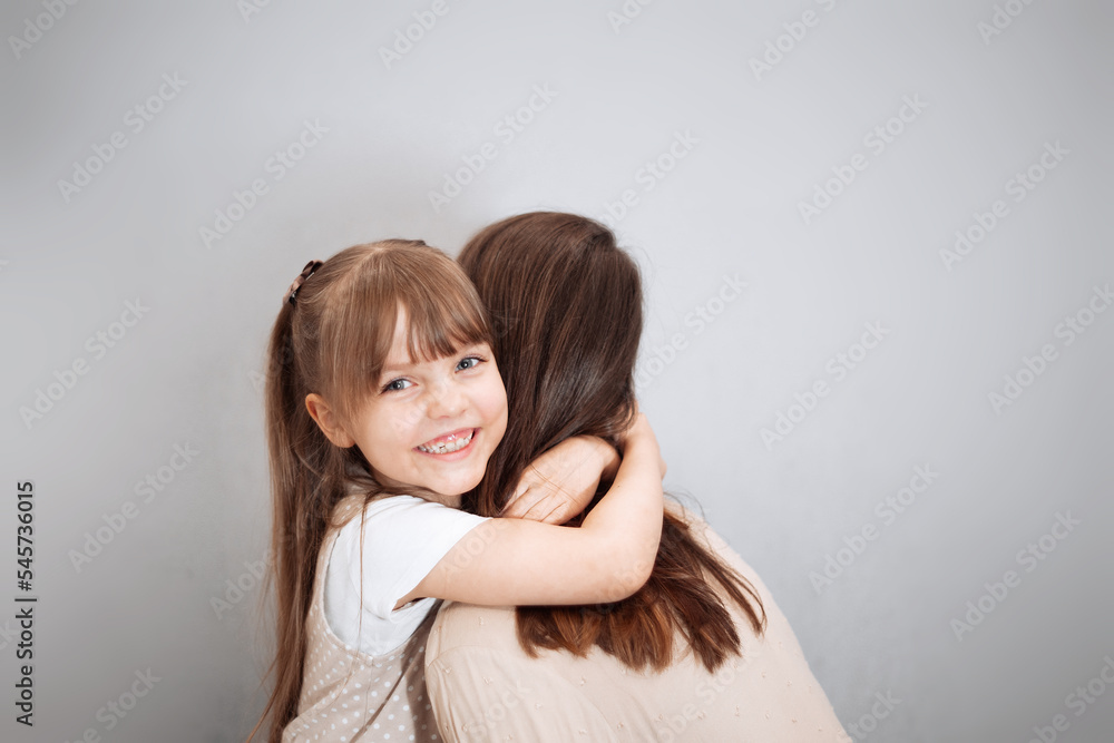 Young mom and her charming cute little daughter are hugging and smiling on a gray background. Concept for mother day Young mom and her charming cute little daughter are hugging and smiling on a gray background. Concept for mother day