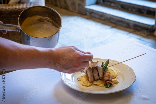 Hand of person adding sauce to the served beef with potatoee photo