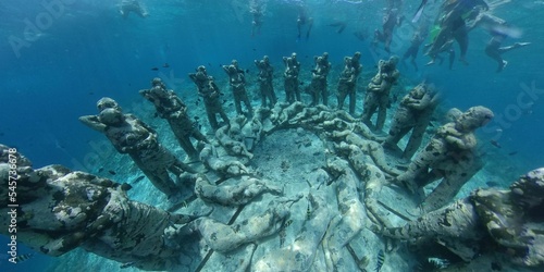 Underwater scenery with sunk old sculptures covered in moss and people scuba diving in Bali