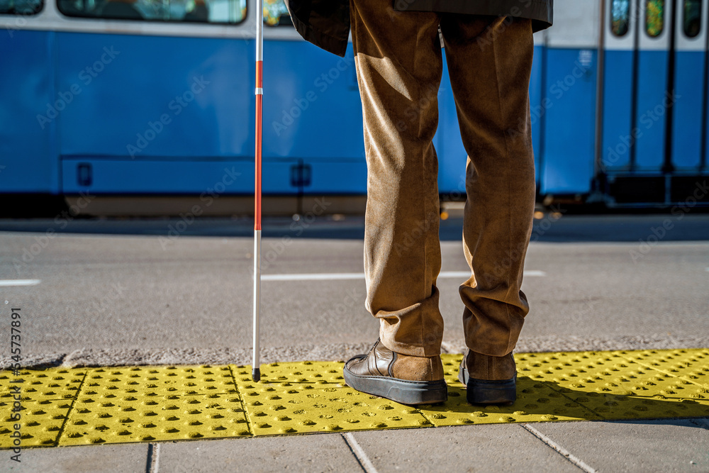 Close-up of a blind man with a cane stopped on a tactile tile in front of a tram obstacle Close-up of a blind man with a cane stopped on a tactile tile in front of a tram obstacle