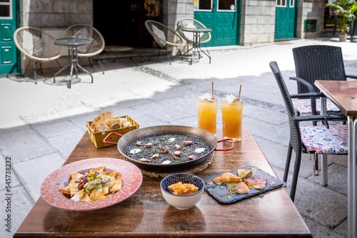 Closeup of a dinner table with Arros Negre, fried chicken, nachos, pita bread and cocktails photo