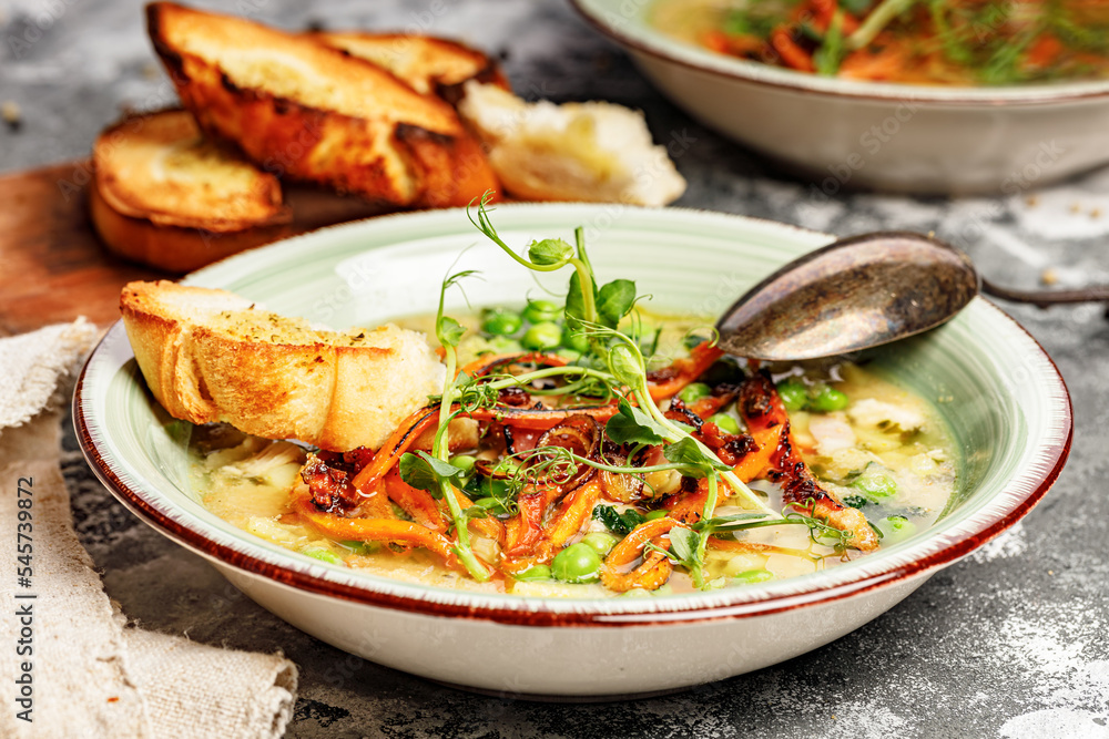 Close-up delicious appetizing vegetable soup with green peas, carrots and fried bacon and garlic croutons.