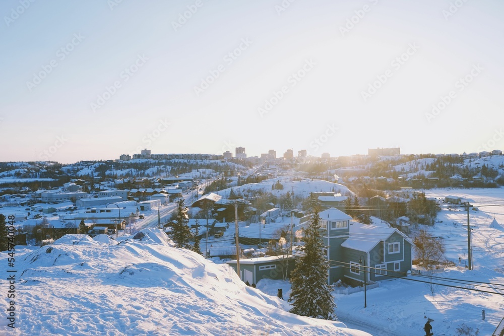 Winter landscape in small village with pine trees, hills and residential houses covered with snow