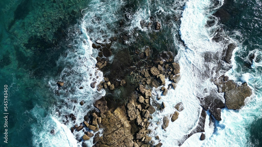 Obraz premium Aerial top view of huge rocks on ocean shore, turquoise strong waves hitting on stone