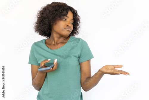 Doubtful young woman with smartphone pointing at copyspace. Indignant African American female model making decision. Studio shoot, emotion, advertisement, concept