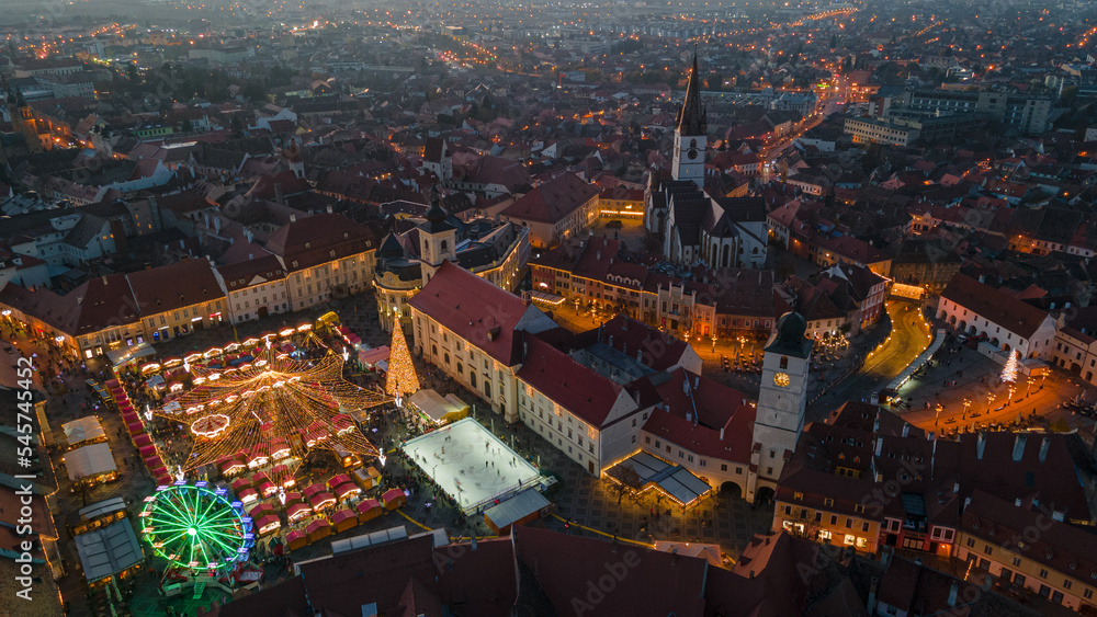 Landscape photography of Sibiu city center with the Christmas Fair, shot from a drone at higher altitude, at sunset with the city lightning on. Birds eye view over cityscape of Sibiu, Romania.