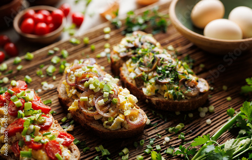 Sandwiches with scrambled eggs and various vegetables, focus on on the sandwich with onion rings  on a wooden plank