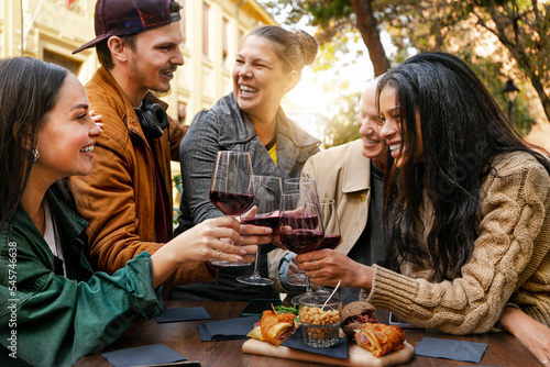 Happy young friends toasting red wine  together at pub- Group of people having fun at restaurant bar eating food and drinking  . Focus on the glasses. Friendship Dinning concept- youth culture 