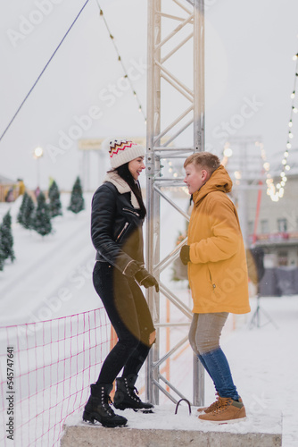 Caucasian mother and son in warm cozy clothes walk outdoors on festive city streets. Family walks at the fair as snow falls. Cold happy winter day. Holidays, Christmas, New Year, love concept.