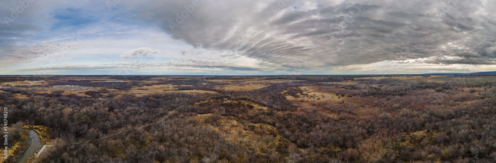 Aerial panorama of a dry prairie setting with a small stream under a sky with interesting clouds
