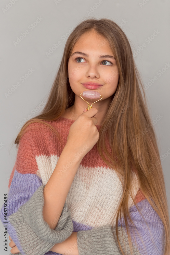 Cute teenage girl posing with face skin care roller, self-care routine Cute teenage girl posing with face skin care roller, self-care routine