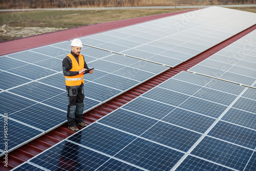 A supervisor is standing on the roof and checking on solar panels over tablet. photo