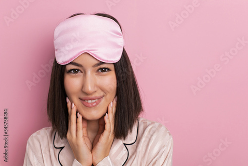 Obraz na płótnie Porter is a beautiful young woman of oriental appearance standing in pink pajamas and a sleeping mask in the bedroom. suffers from insomnia. w salonie