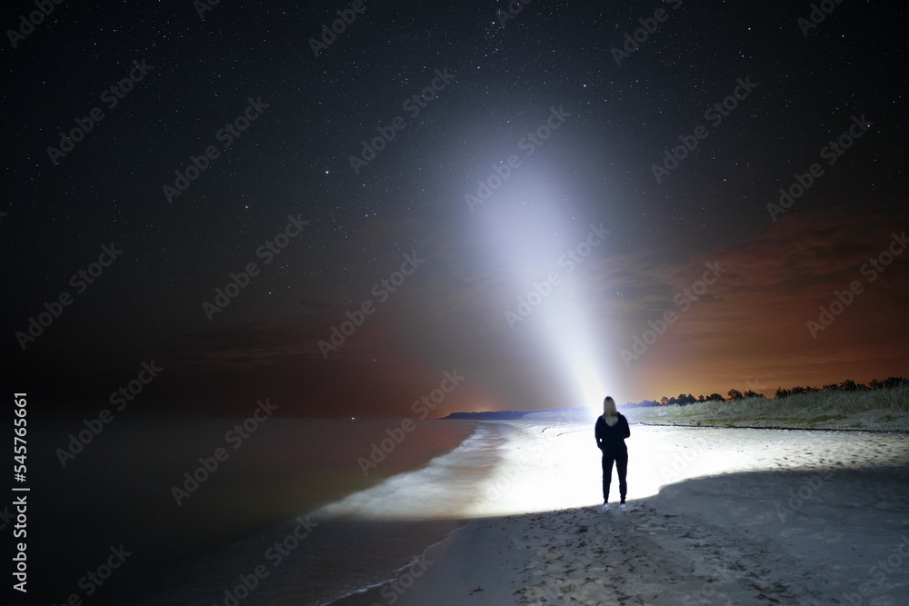 Night scene, a girl with a flashlight on the sea beach, a beautiful starry sky.
