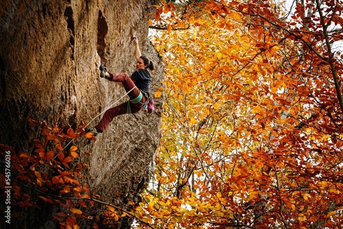 Woman Rock Climbing a steep cave against vibrant orange autumn falling leaves.