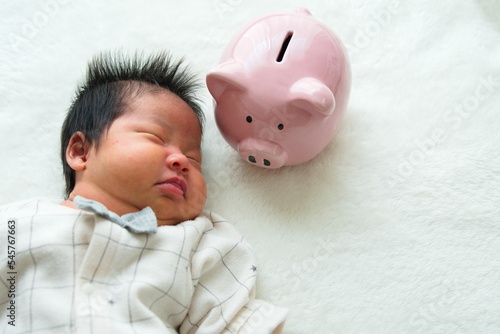寝ている産後1か月0歳の新生児と豚の貯金箱を置いた左寄りの写真 photo