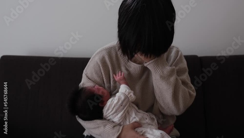 大泣きしている産後1か月0歳の新生児を母親が抱っこしながら顔に手を当てている様子の動画 photo