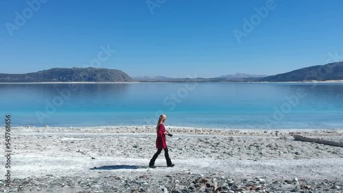drone footage of a blonde woman walking on the white sands of Salda lake, first scene slides aside the woman then gets front and elevates to have to whole lake scene