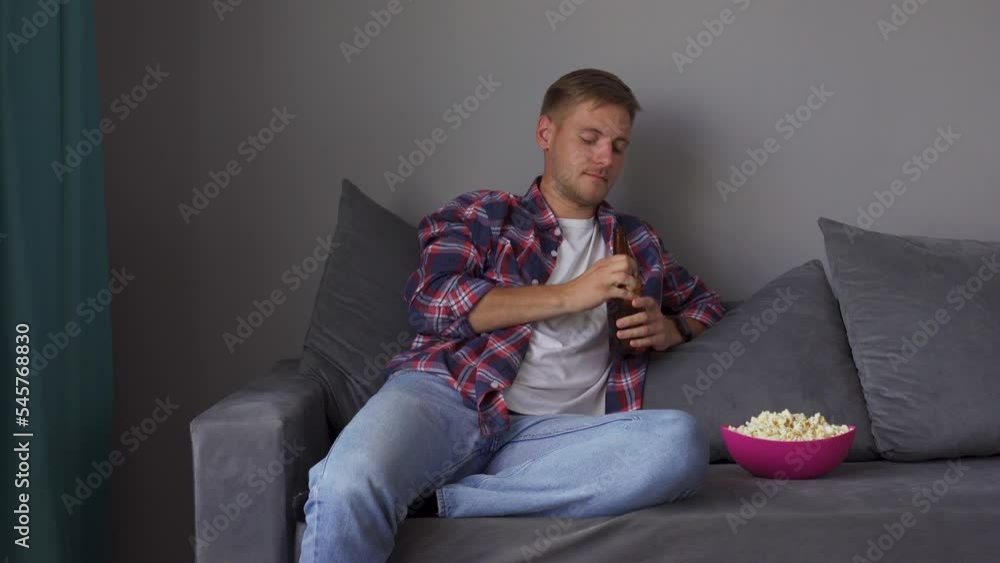 A young man drinking beer while sitting on the couch. Concept of free time, sport and entertainment A young man drinking beer while sitting on the couch. Concept of free time, sport and entertainment