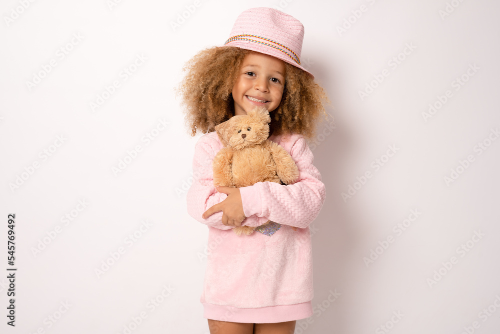 Little child girl wearing straw hat is hugging teddy bear isolated over white background. Little child girl wearing straw hat is hugging teddy bear isolated over white background.