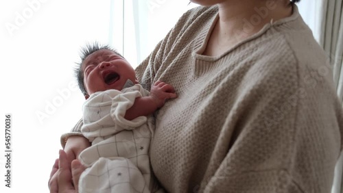 産後1か月0歳の新生児が泣いているところ母親が抱っこしてあやしている横からの動画 photo