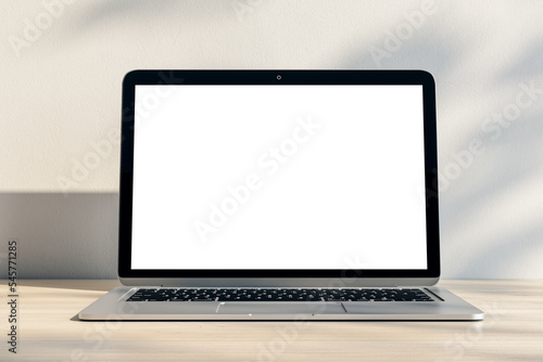 Closeup of modern laptop with blank white screen and place for your logo or text on light wooden table and sunlit wall background. 3D rendering, mock up