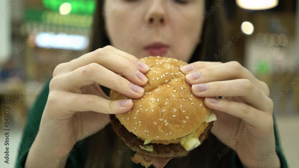 Focus on burger closeup. Woman biting a big burger at the food court Focus on burger closeup. Woman biting a big burger at the food court