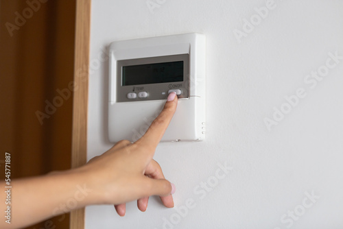 Close-up of a young woman's hand pressing the on/off button of the air conditioner or heater