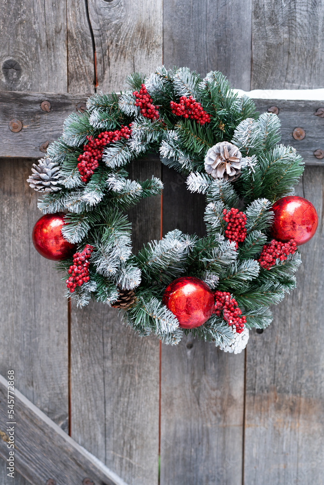 Christmas wreath of spruce twigs made of glass balls of red color hanging on wooden fence of village house. Close-up new years decorations for gate to country cottage to decorate for winter holidays Christmas wreath of spruce twigs made of glass balls of red color hanging on wooden fence of village house. Close-up new years decorations for gate to country cottage to decorate for winter holidays